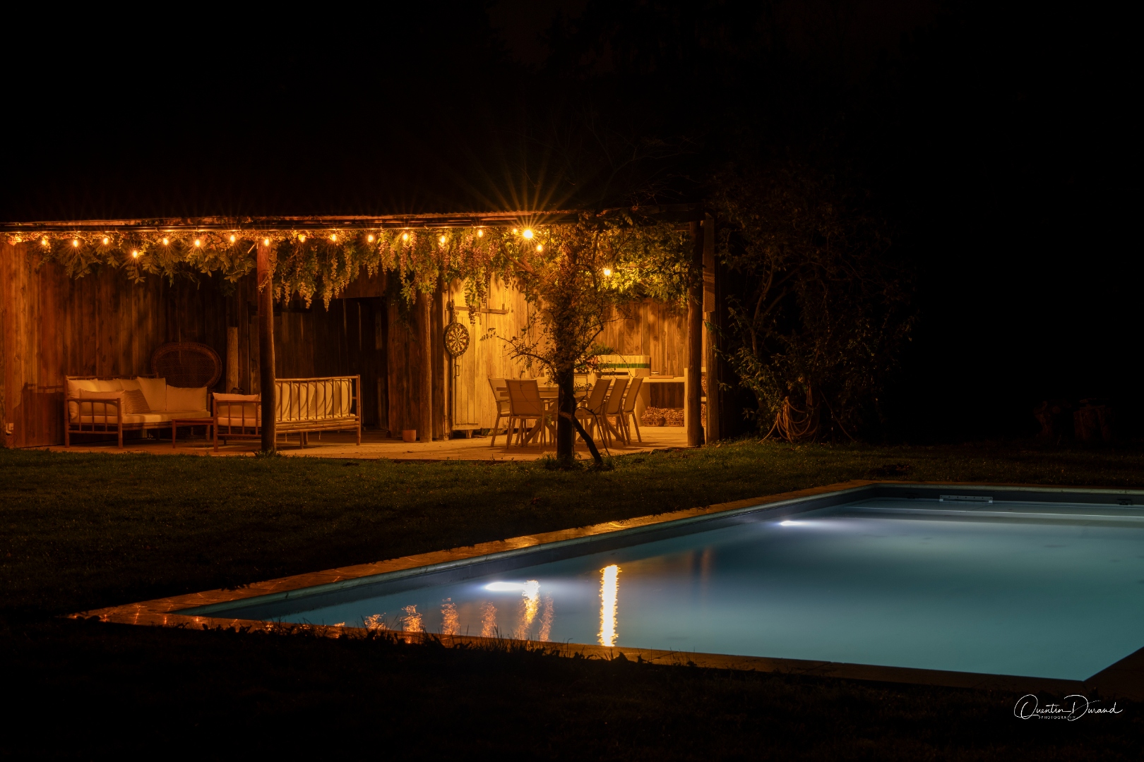Pool illuminated at night with string lights on the pergola